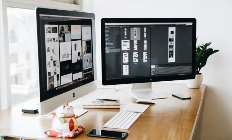 Two Imac's With Keyboard and Phones on Desk